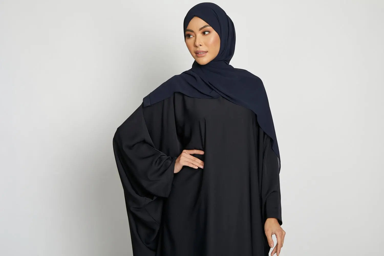 Woman wearing a black abaya and navy hijab on a white background