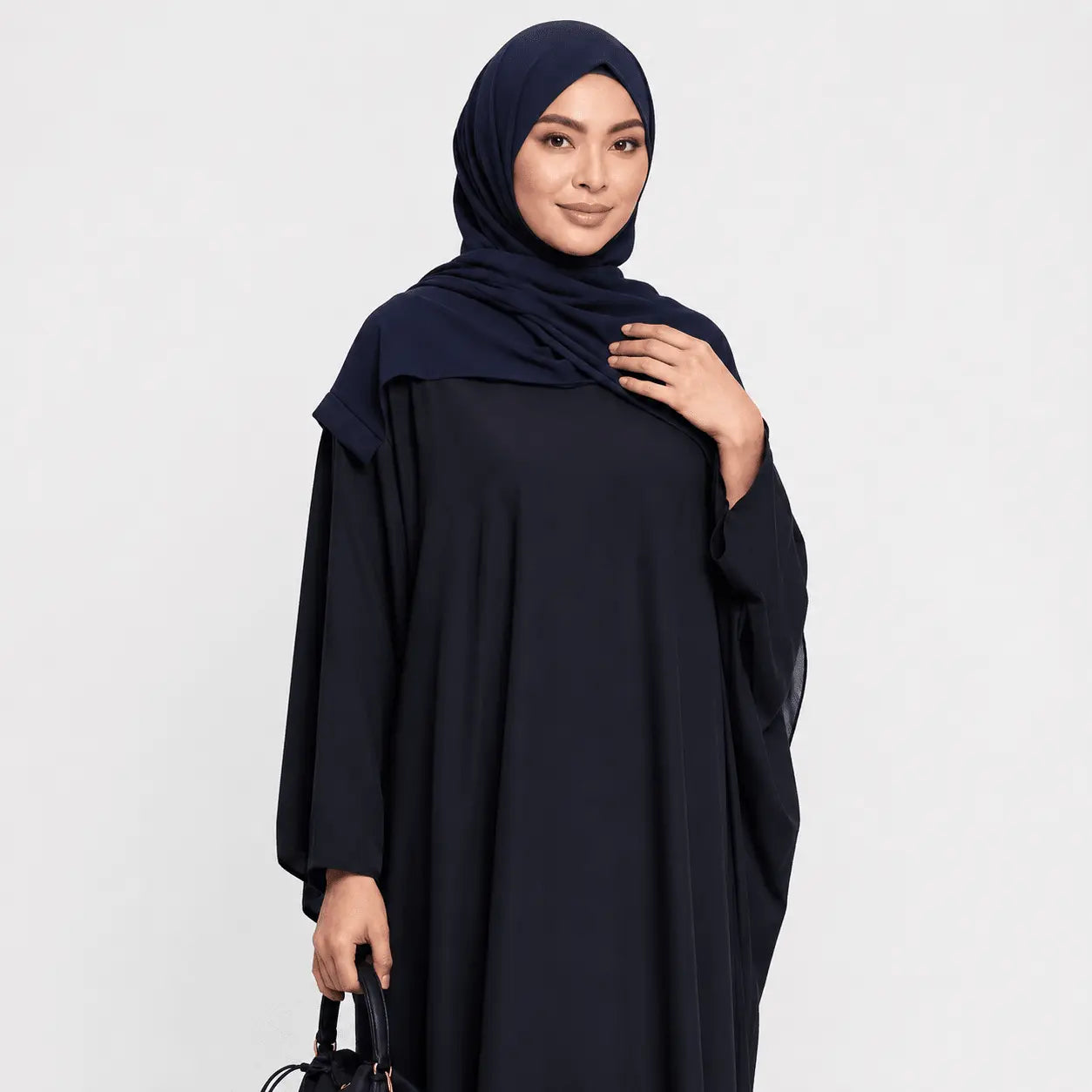 Woman wearing a black abaya and navy hijab on a white background