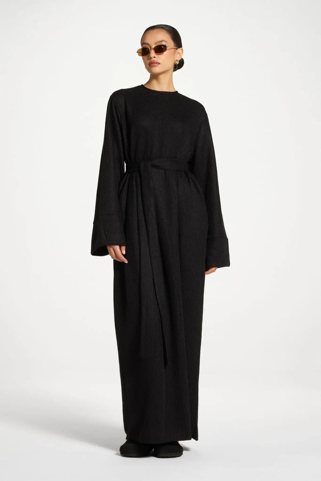 Woman wearing a black long-sleeve dress with a belt on a white background