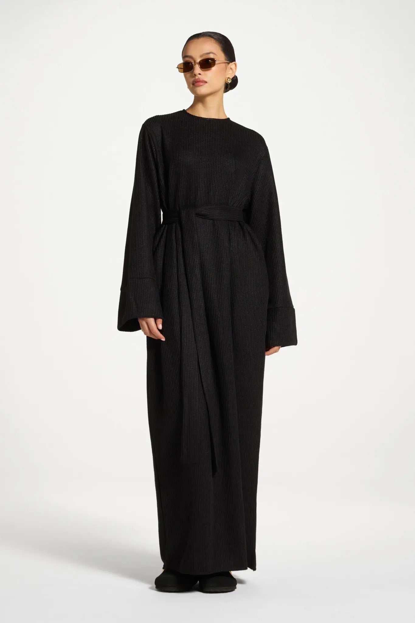 Woman wearing a black long-sleeve dress with a belt on a white background