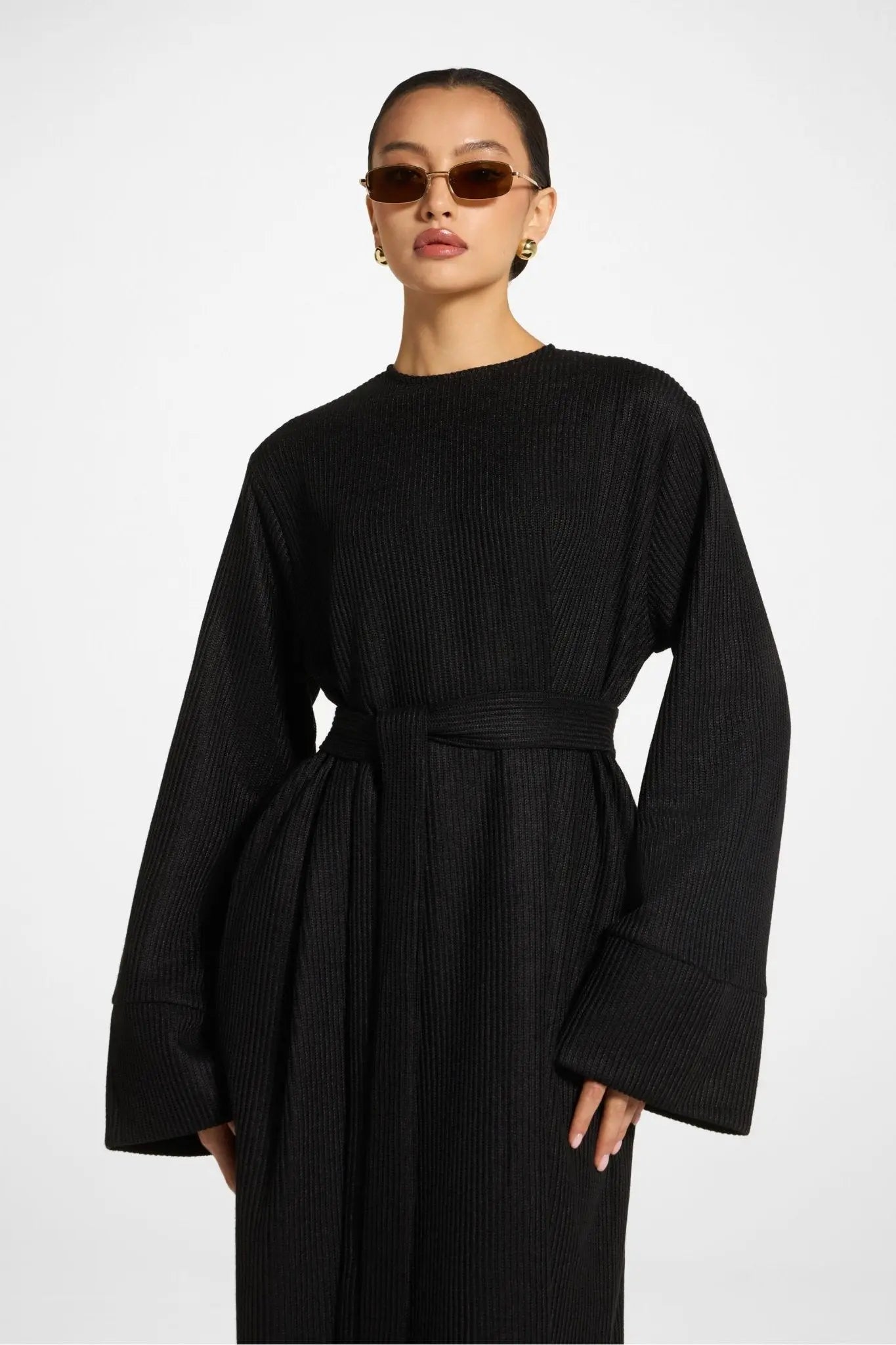 Person wearing a black ribbed sweater with wide sleeves on a white background