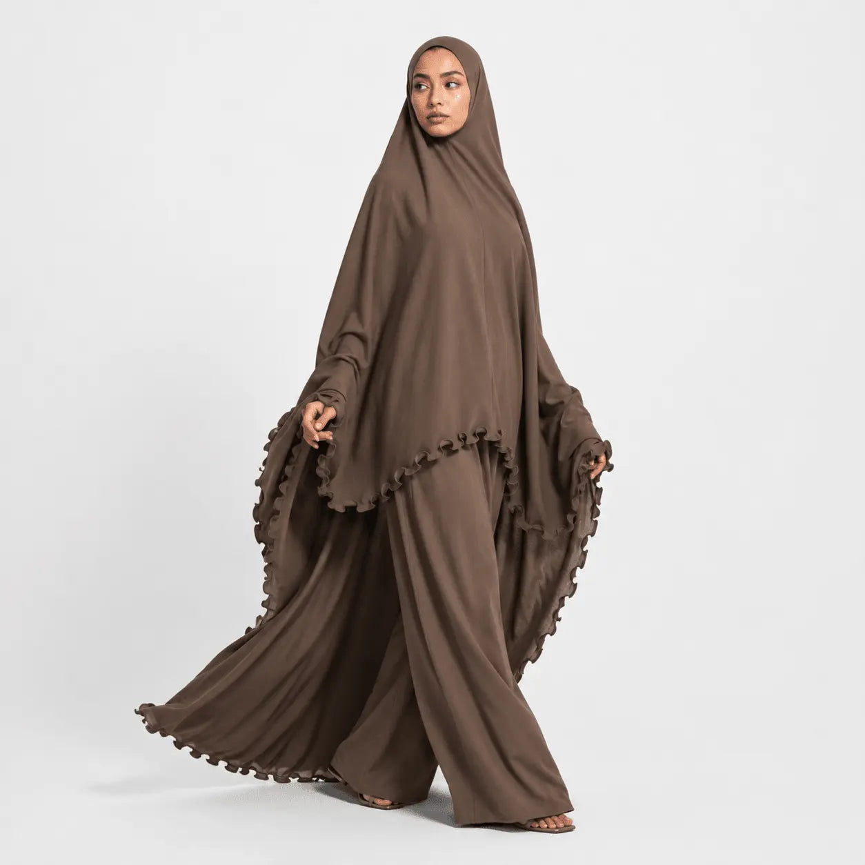Woman wearing a brown abaya with ruffled details on a white background