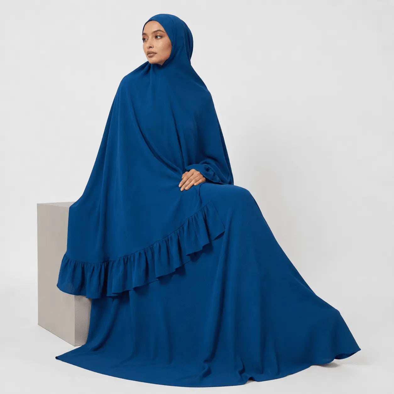 Woman wearing a blue abaya with ruffled details on a white background
