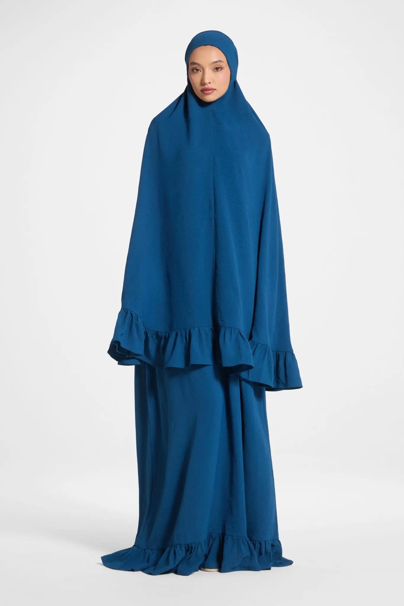 Woman wearing a blue dress with a matching hijab on a white background