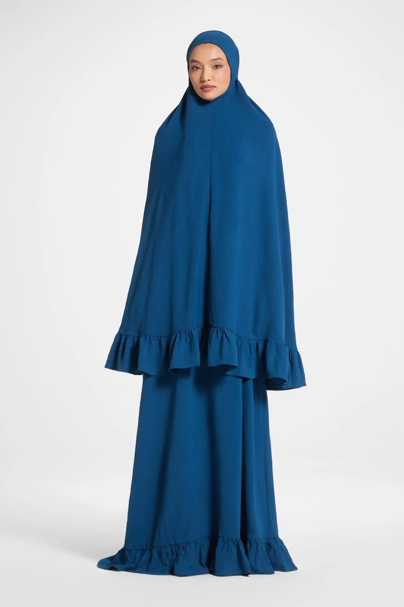 Woman wearing a blue dress with a matching hijab on a white background