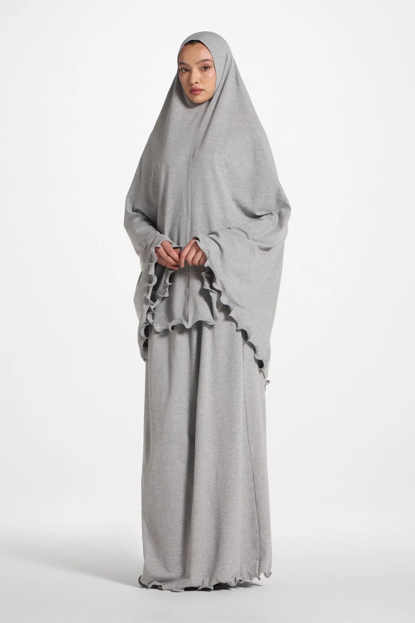 Woman wearing a gray abaya with ruffled details on a white background