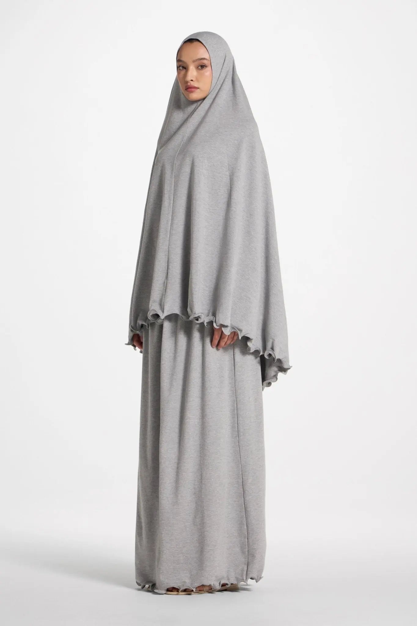 Woman wearing a gray abaya and hijab on a white background