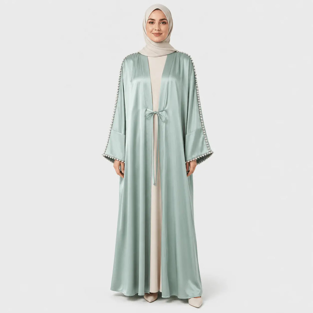 Woman wearing a light green abaya with decorative trim on a white background