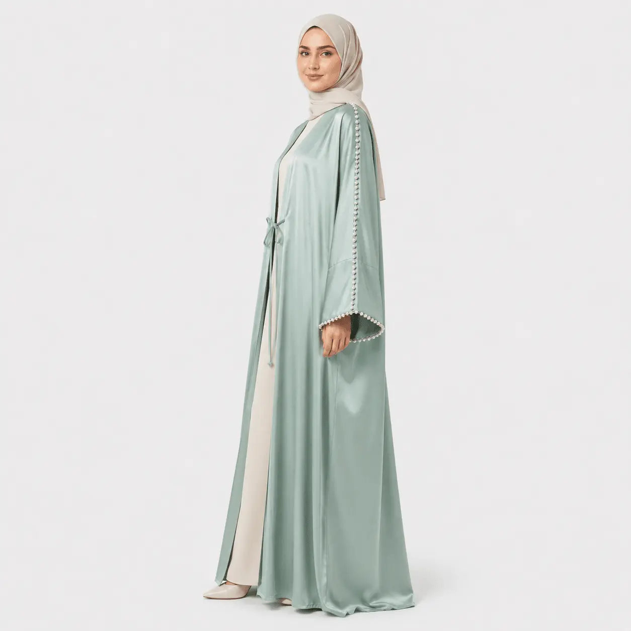 Woman wearing a light green abaya with white trim on a white background