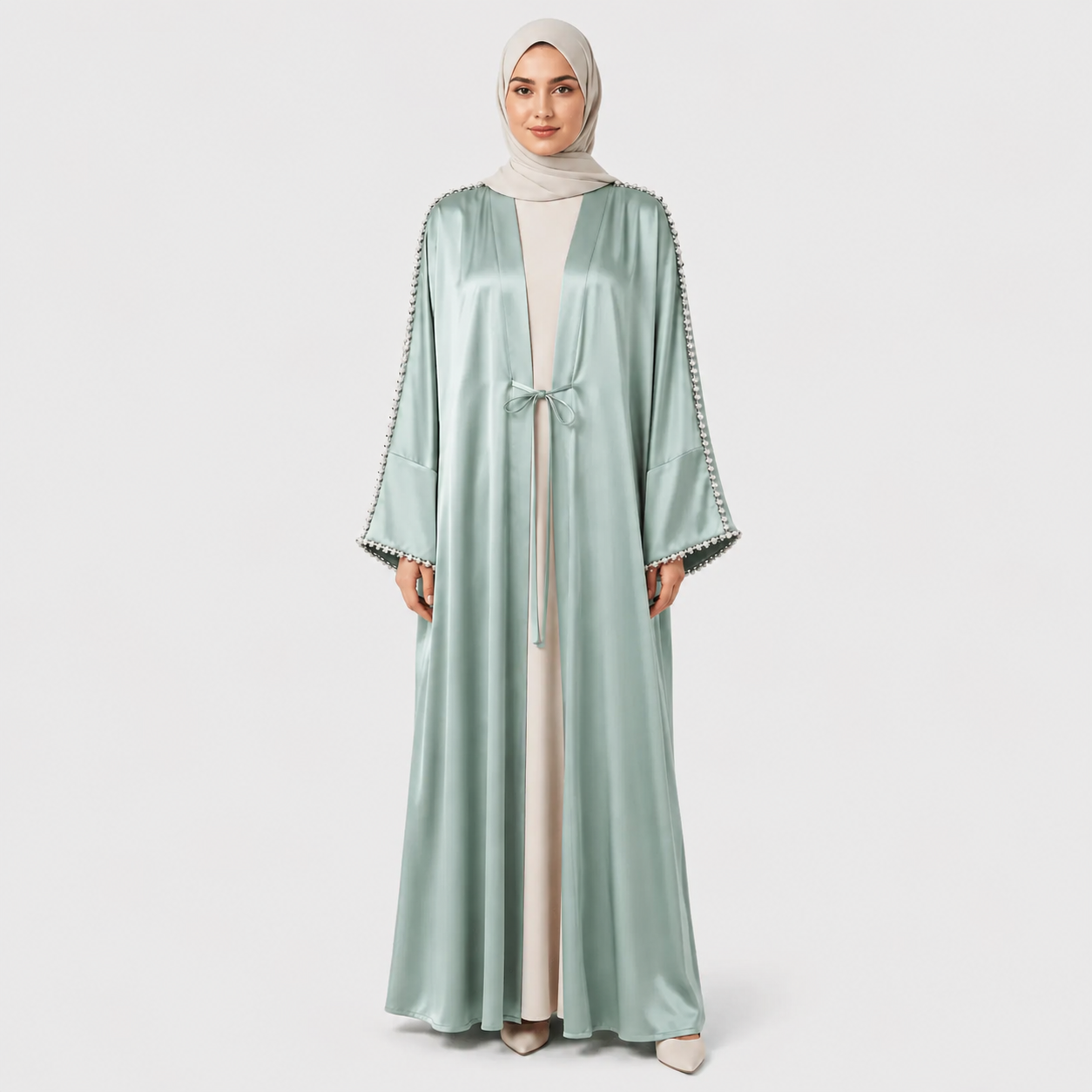 Woman wearing a light green abaya with decorative trim on a white background