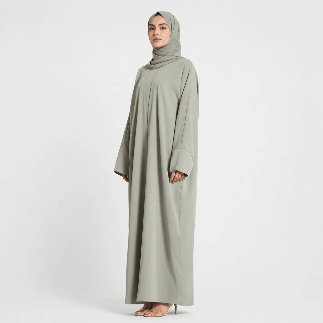 Woman wearing a long, light gray dress with a matching hijab on a white background