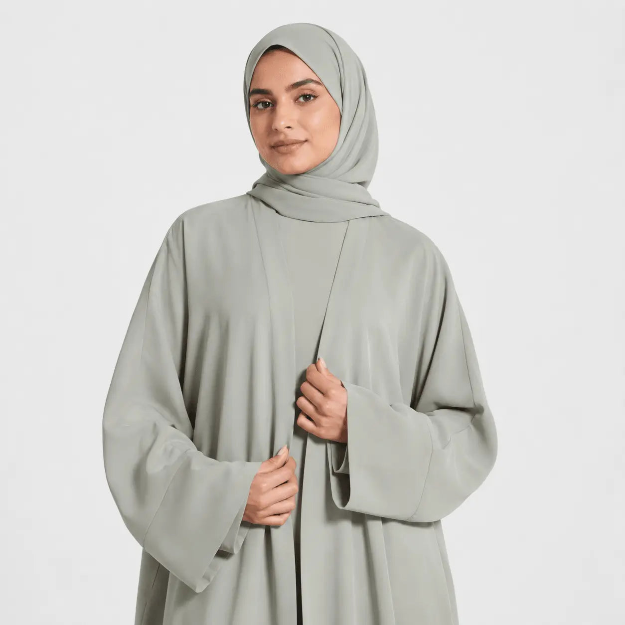 Person wearing a light gray abaya and hijab on a white background