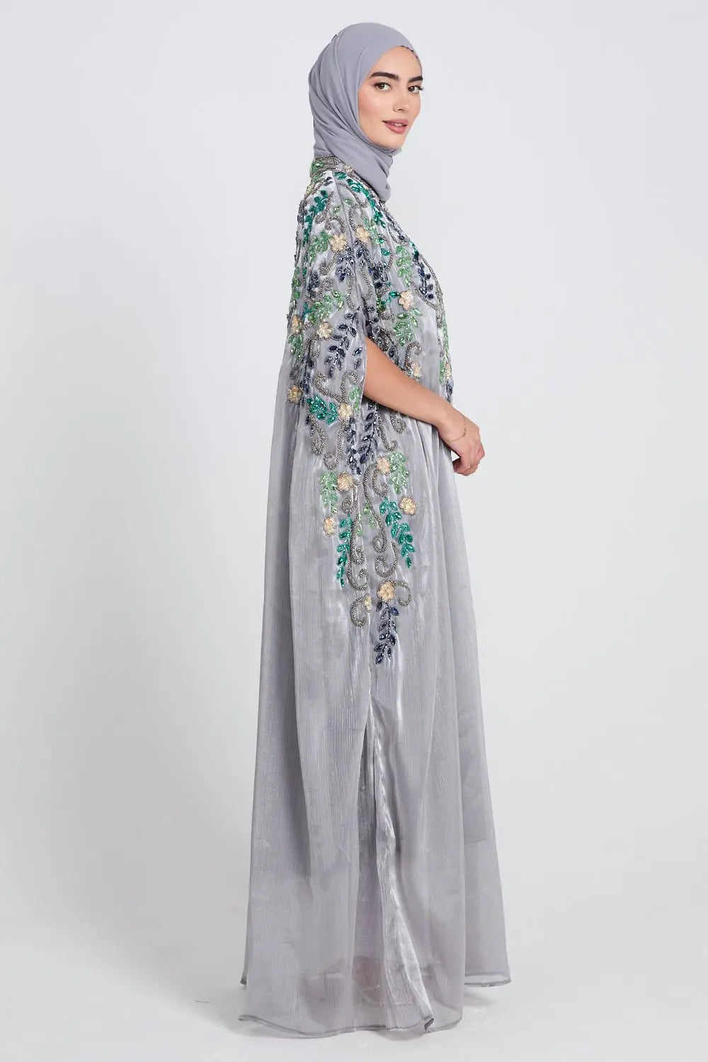 Woman wearing a gray dress with floral embroidery and a matching hijab on a white background