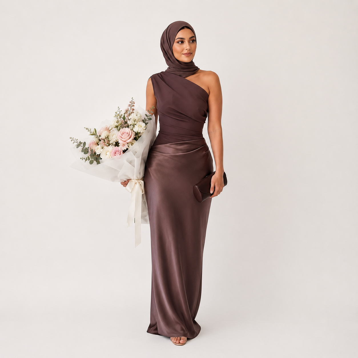 Woman in a brown one-shoulder gown holding flowers on a white background