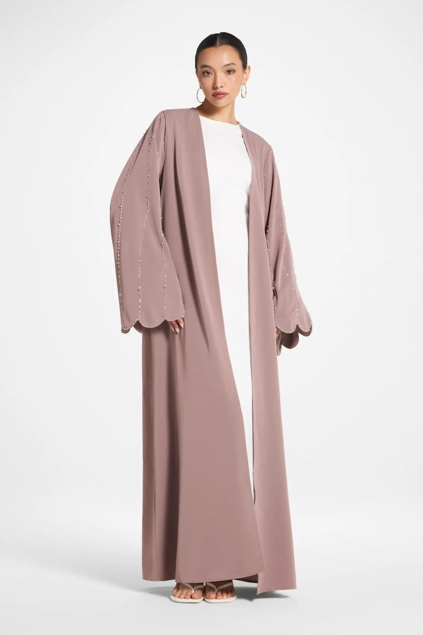 Woman wearing a long mauve cardigan over a white dress on a white background