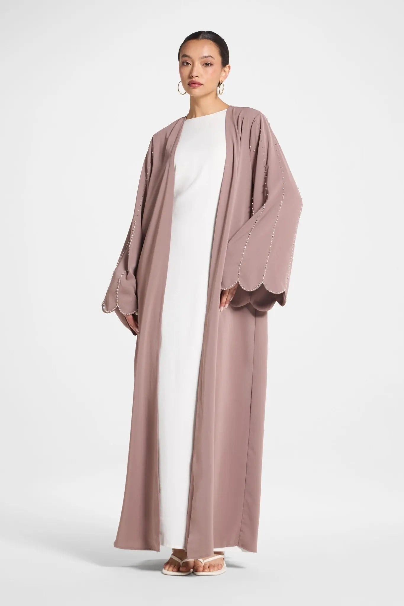 Woman wearing a long, light brown robe over a white outfit on a white background