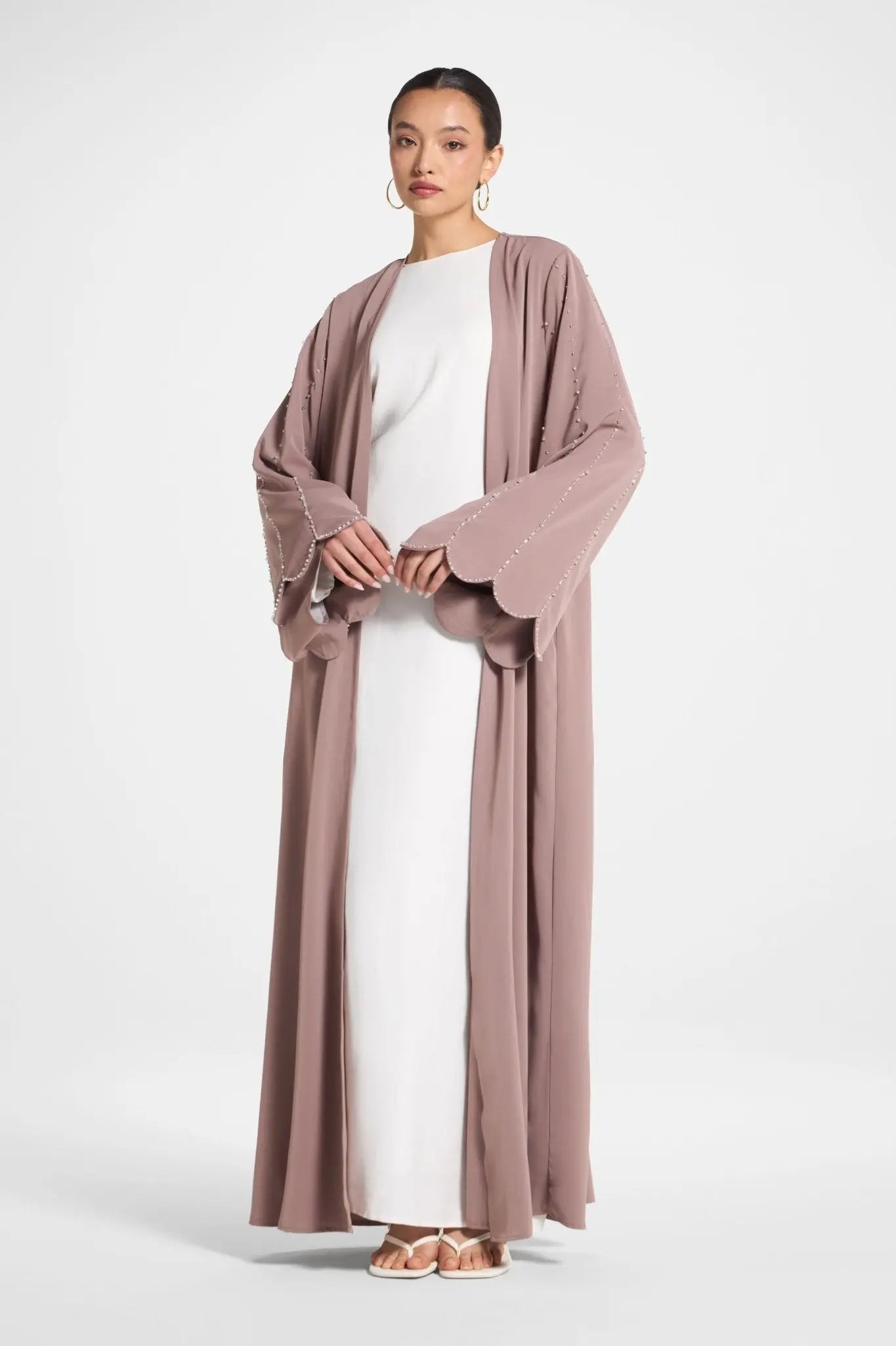 Woman wearing a long, light brown cardigan over a white dress on a white background