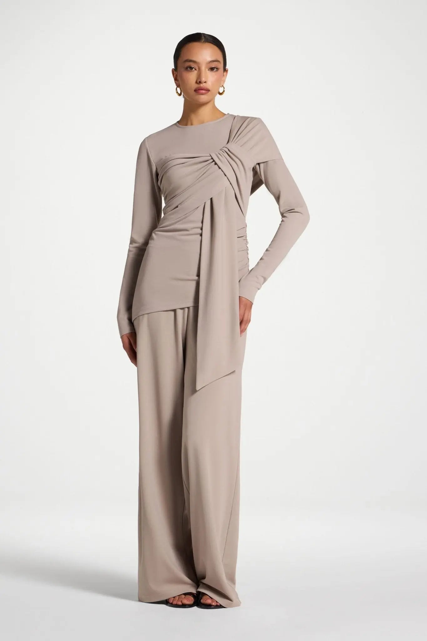 Woman wearing a beige long-sleeve top and wide-leg pants on a white background