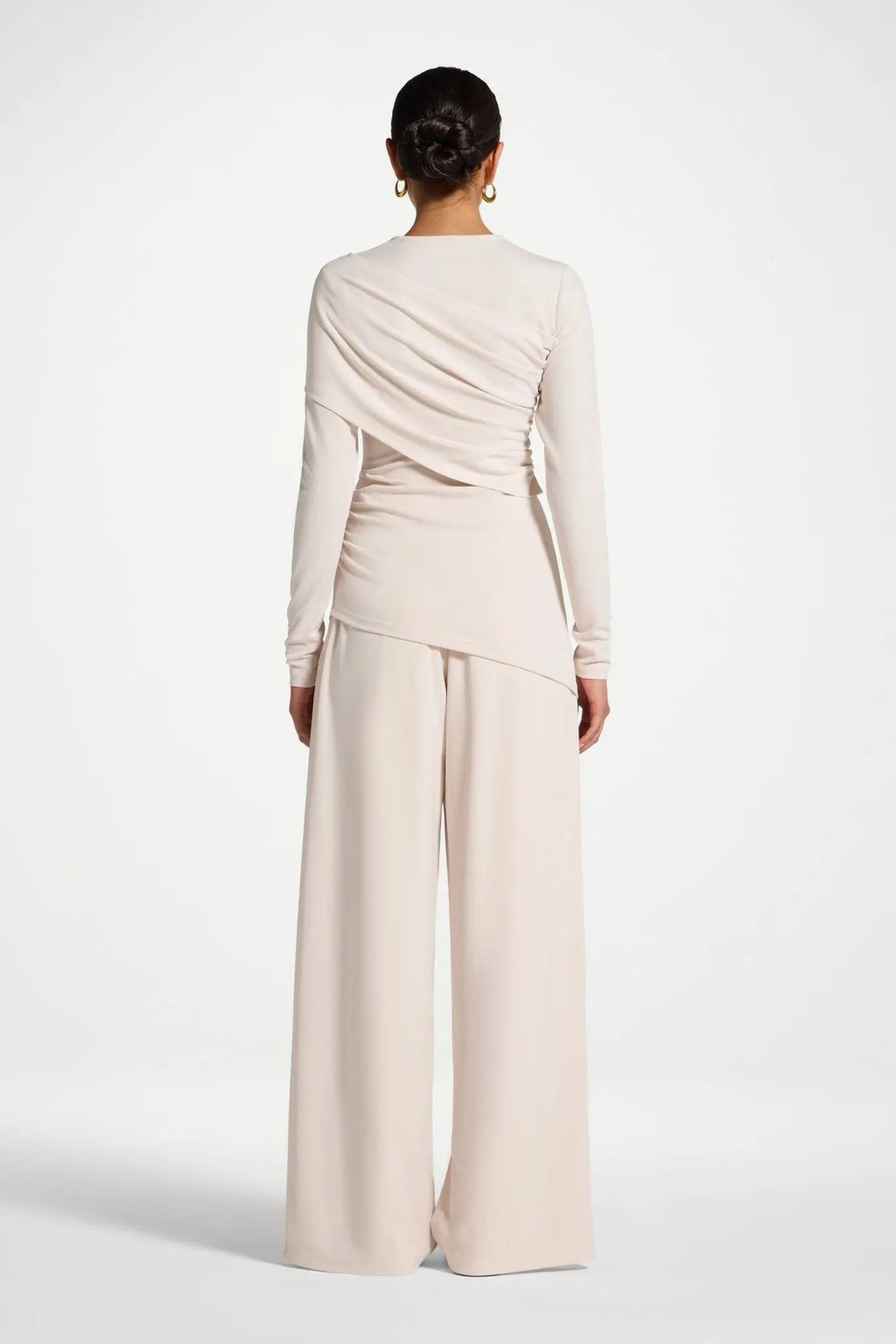 Person wearing a beige long-sleeve top and wide-leg pants on a white background