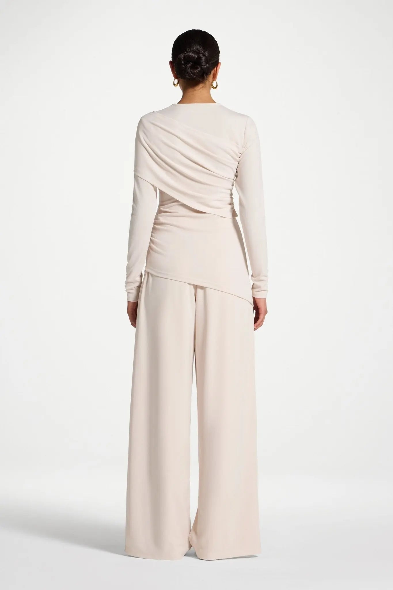 Person wearing a beige long-sleeve top and wide-leg pants on a white background