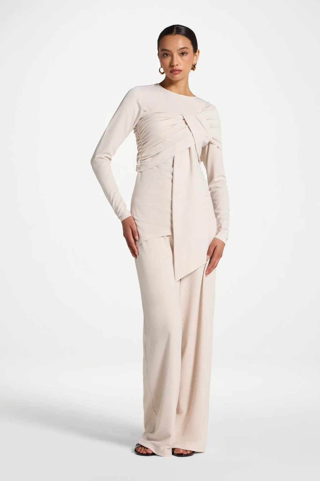 Woman wearing a long, light-colored dress with a draped design on a white background