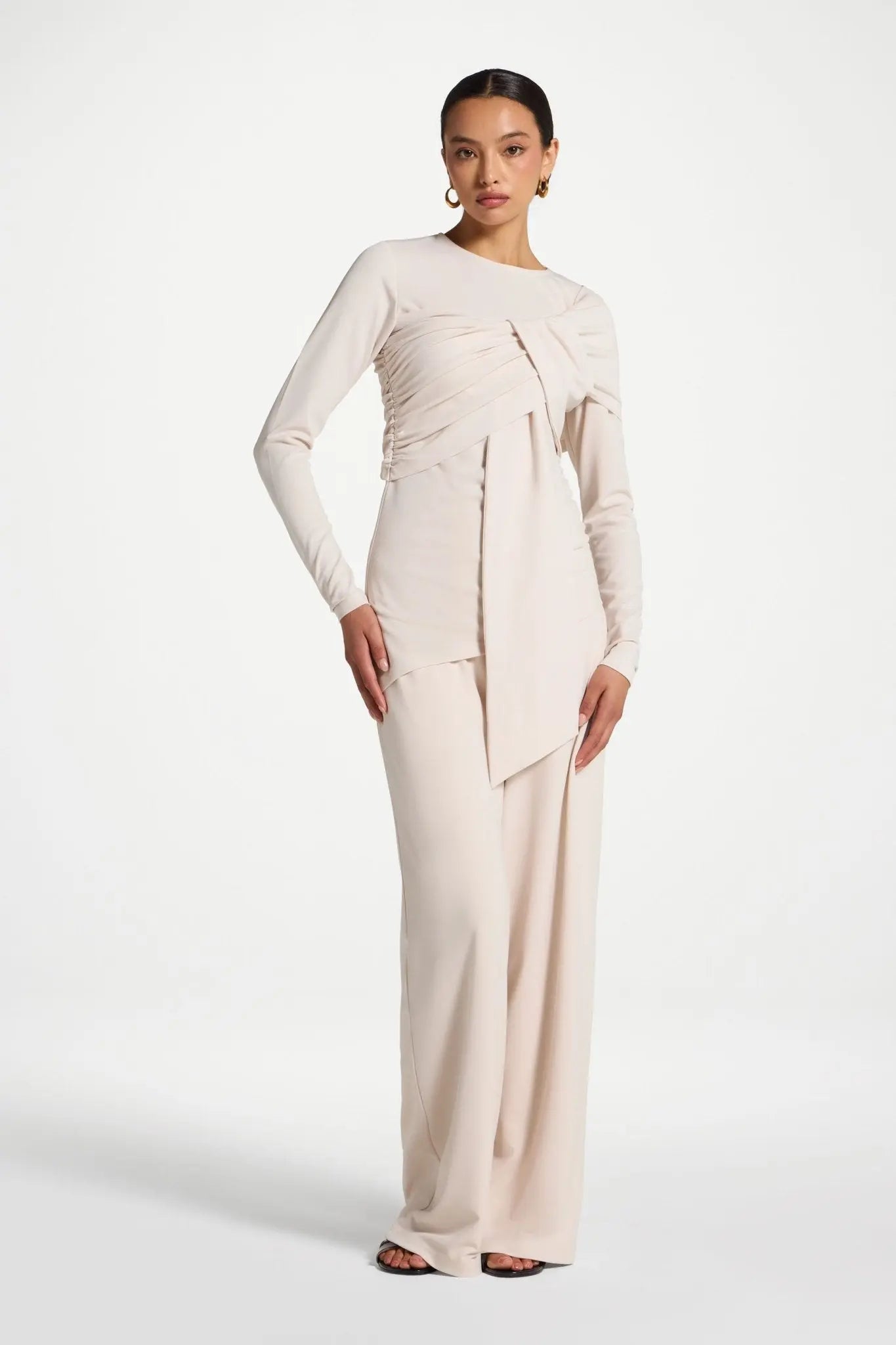 Woman wearing a long, light-colored dress with a draped design on a white background