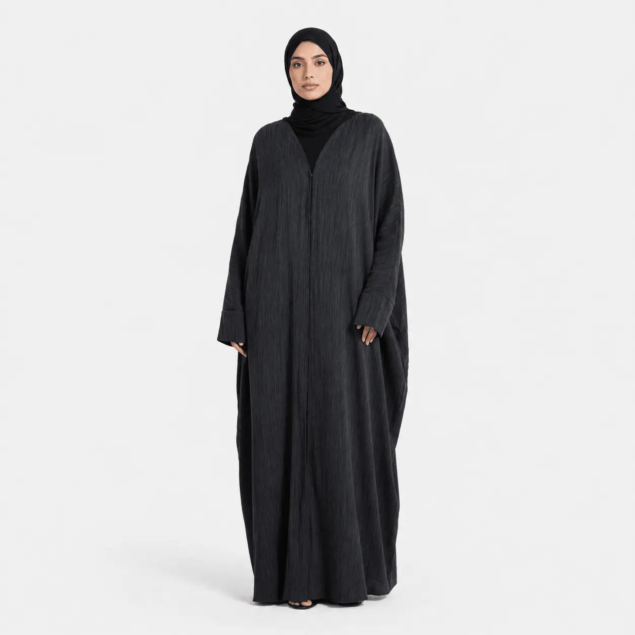 Woman wearing a long black abaya on a white background