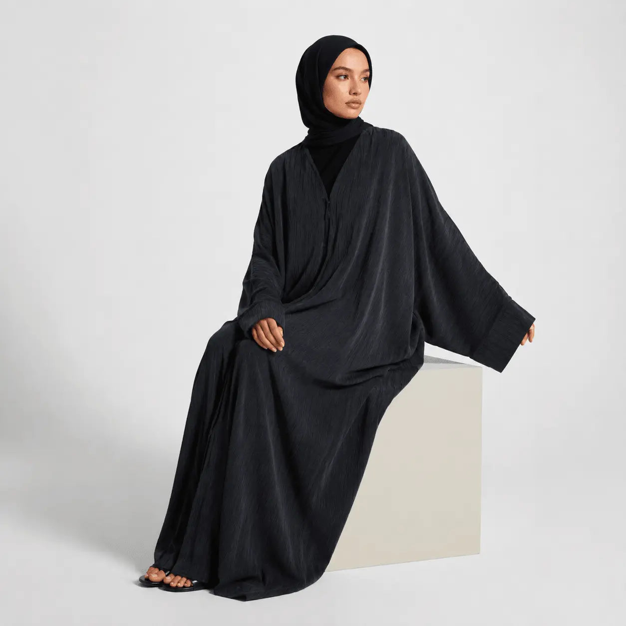Woman wearing a black abaya sitting on a white surface with a light gray background