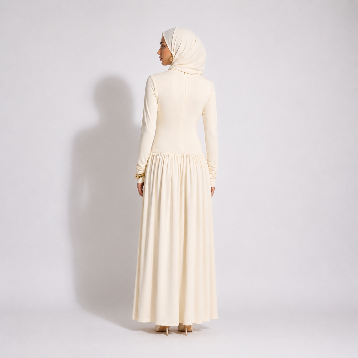 Woman wearing a long cream dress and hijab on a white background