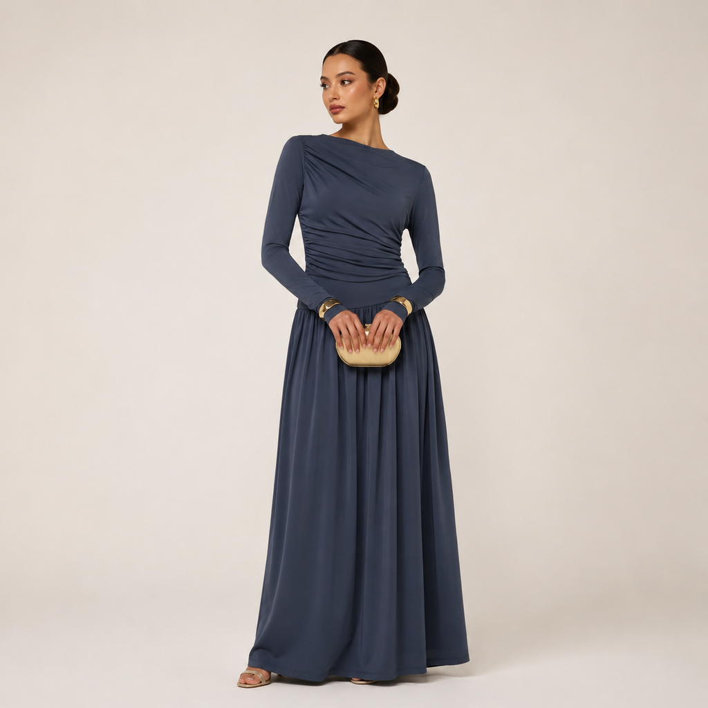 Woman wearing a long blue dress holding a clutch against a beige background