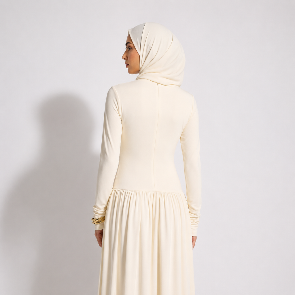 Woman wearing a cream-colored dress and hijab against a plain background