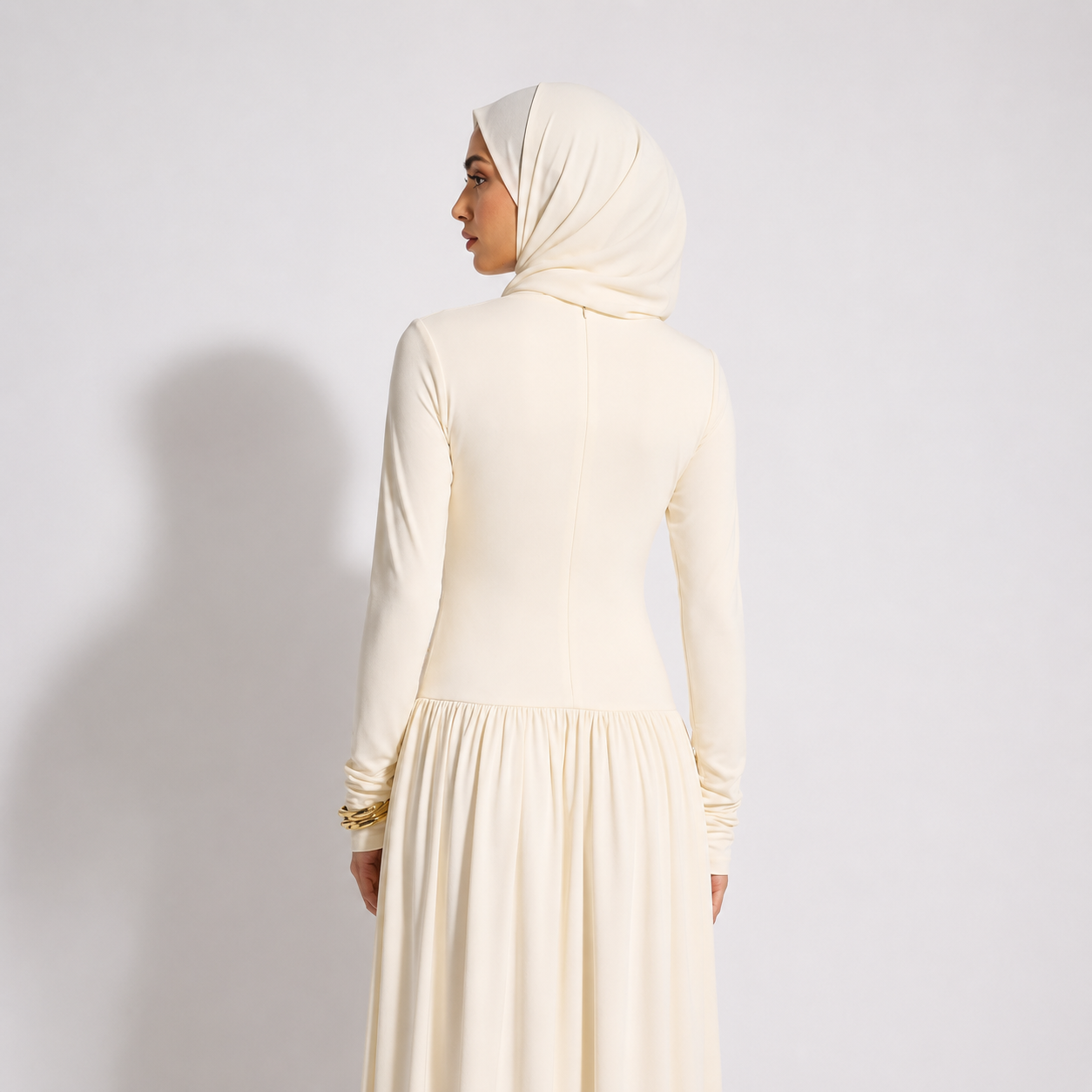 Woman wearing a cream-colored dress and hijab against a plain background