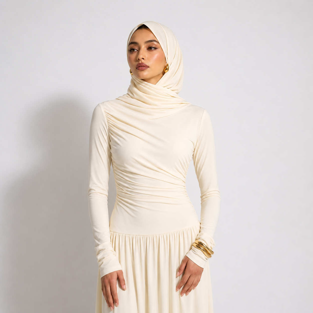 Woman wearing a cream hijab and dress against a plain background