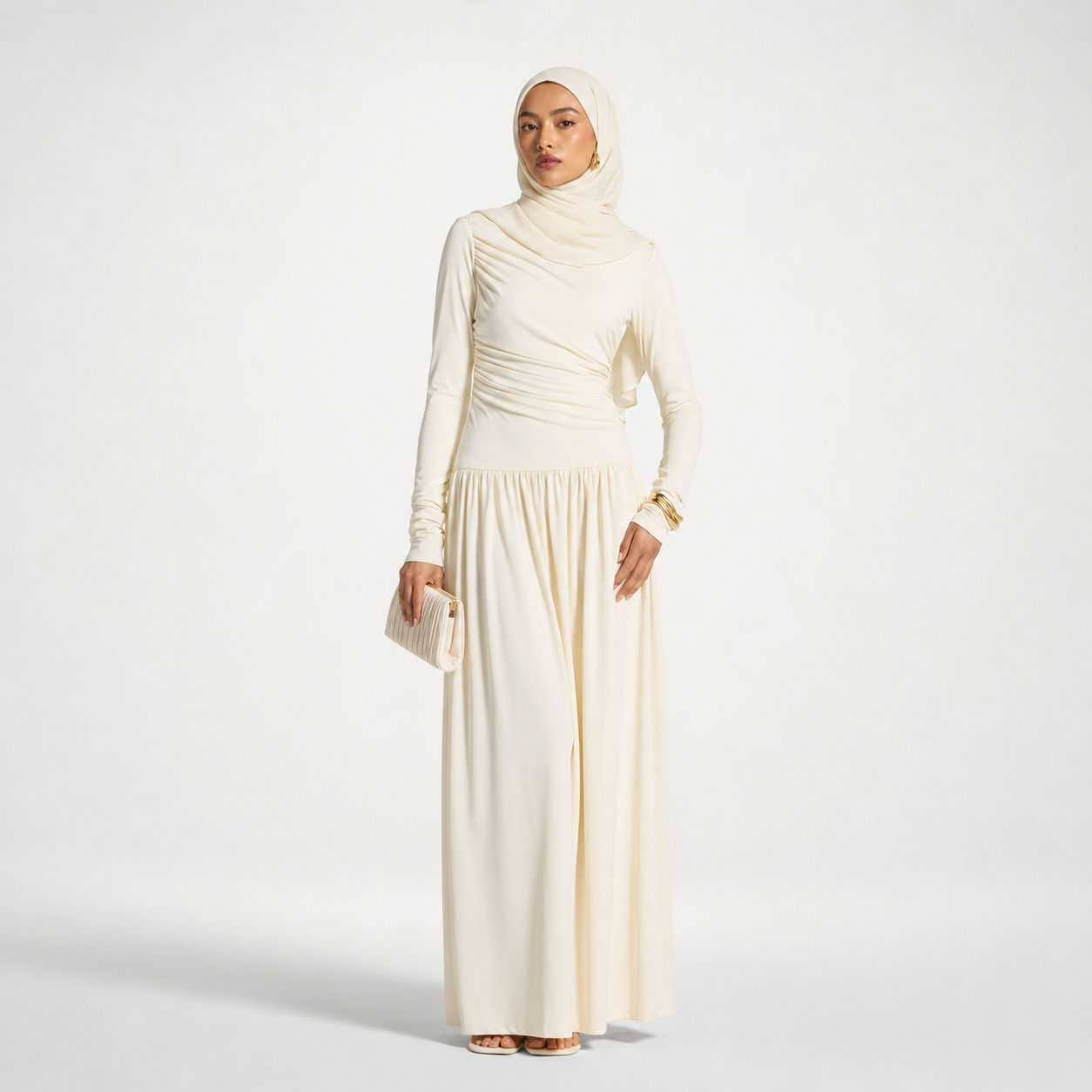 Woman wearing a long cream dress with a matching hijab on a white background
