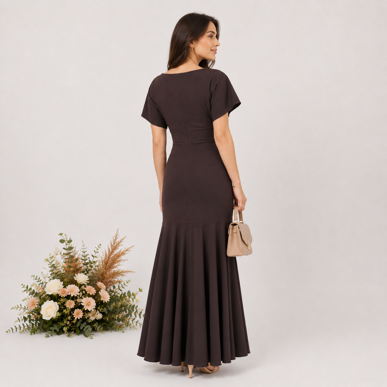 Woman in a brown dress holding a beige handbag with flowers on a light gray background