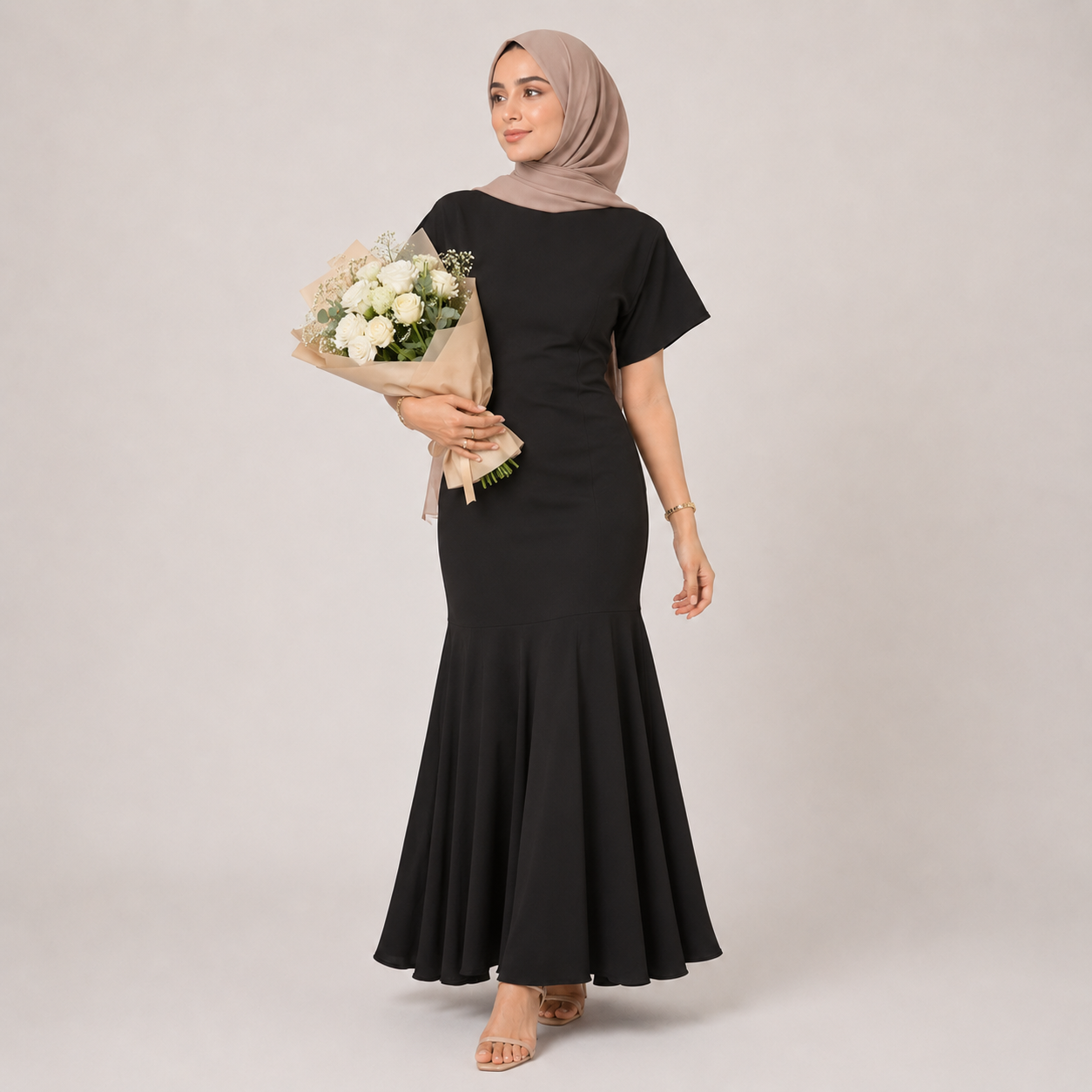 Woman in a black dress holding flowers against a plain background