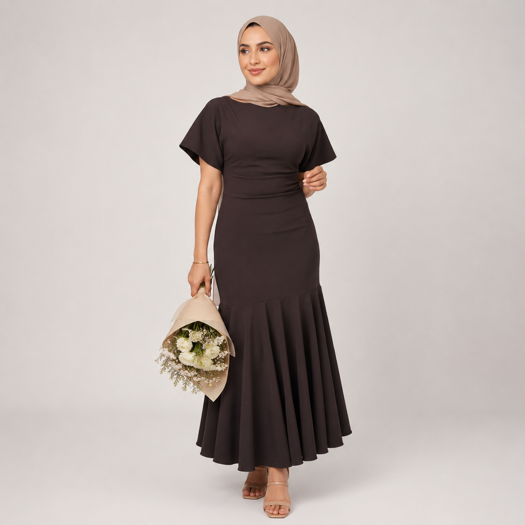 Woman wearing a dark brown dress with a fitted bodice and flared skirt, holding a bouquet of flowers against a plain background.