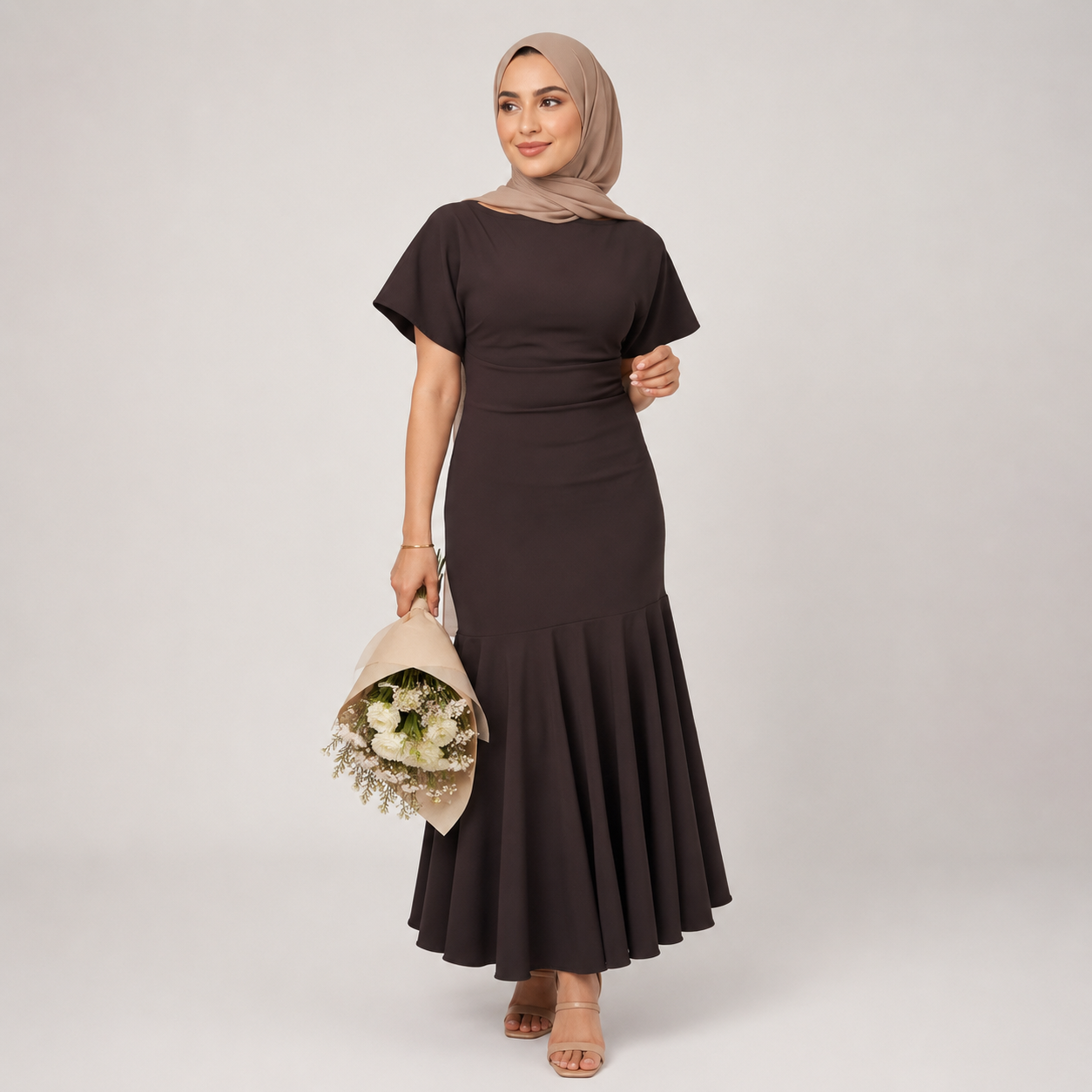 Woman wearing a dark brown dress with a fitted bodice and flared skirt, holding a bouquet of flowers against a plain background.