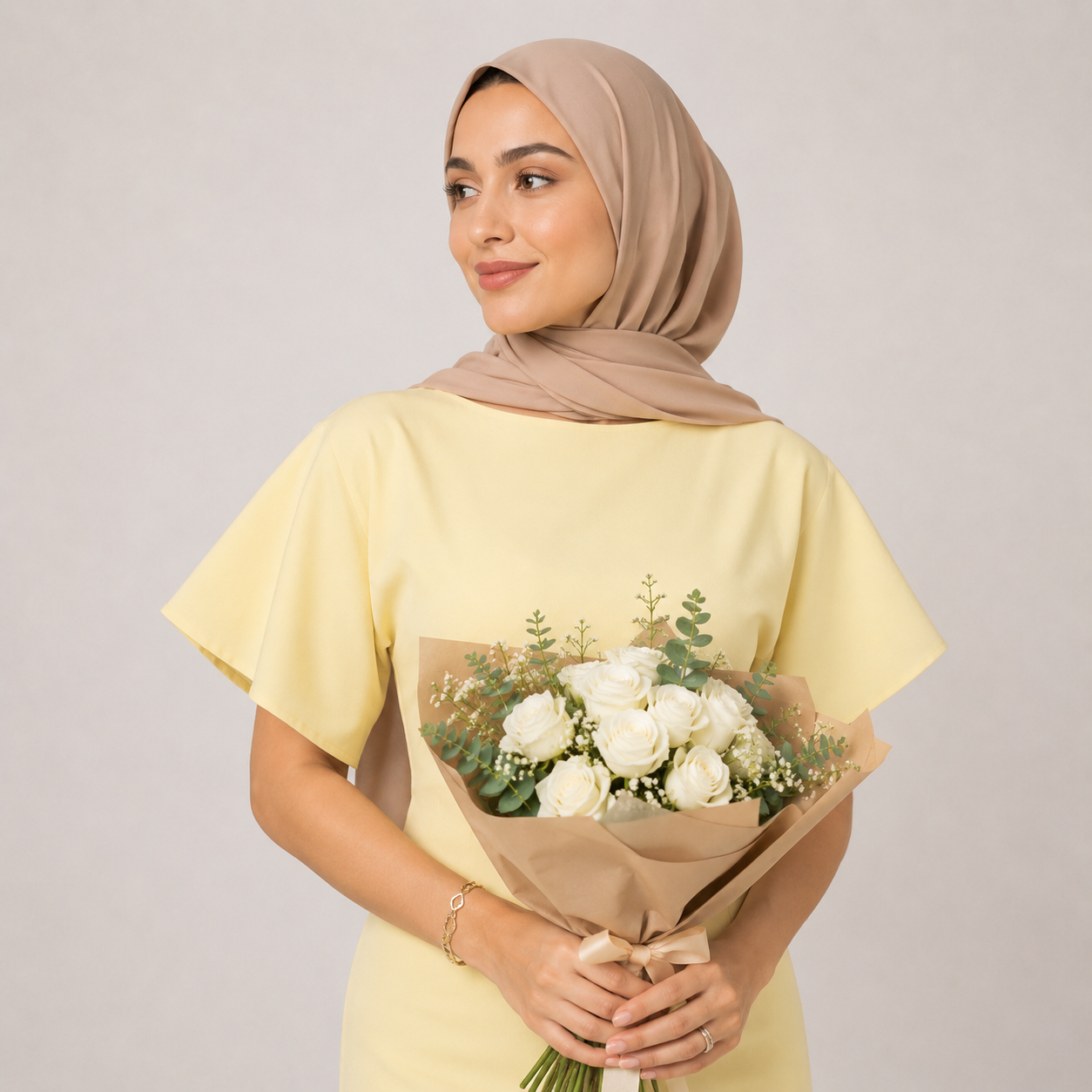 Woman in a yellow dress holding a bouquet of white flowers against a plain background