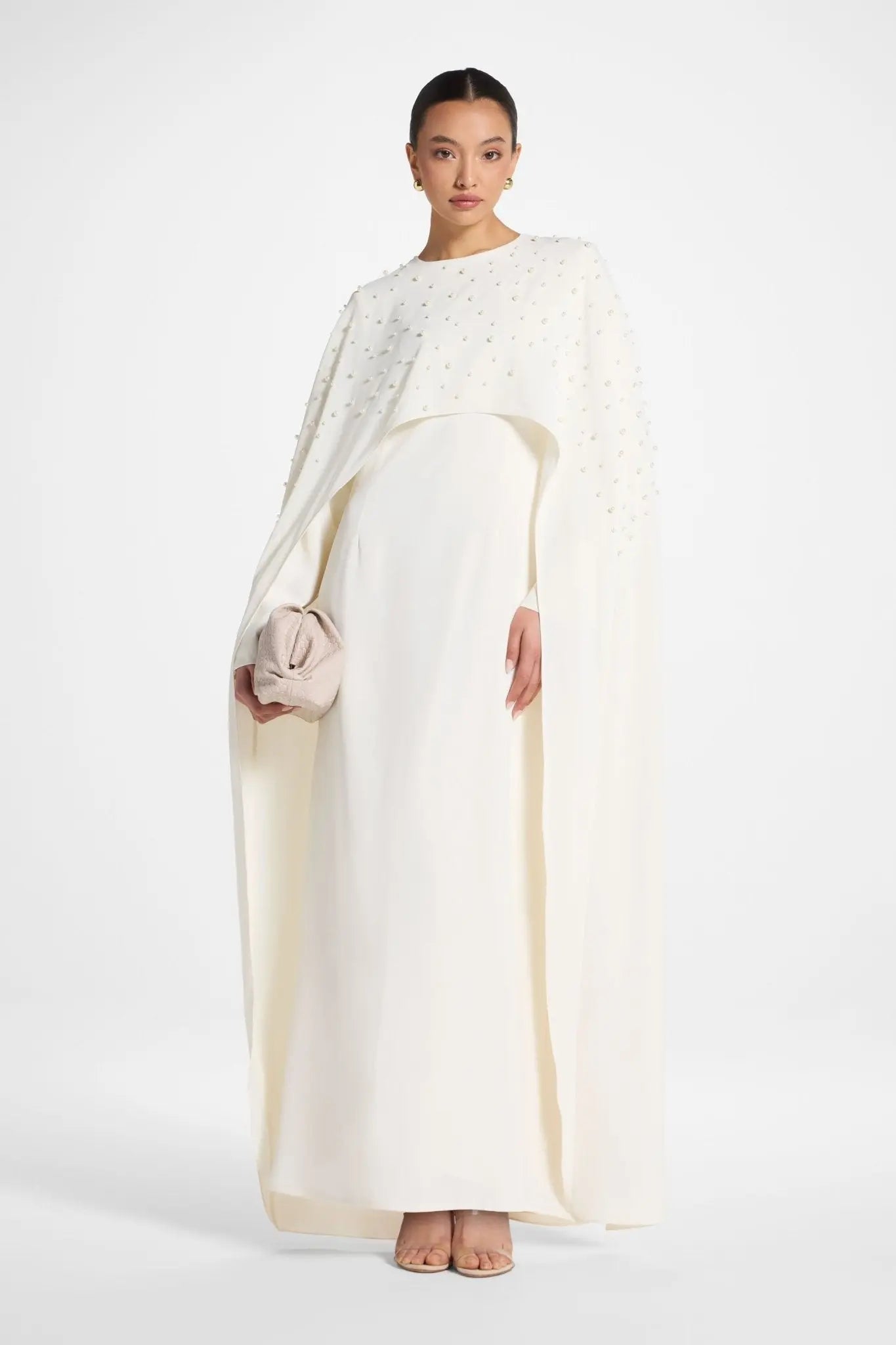 Woman wearing a long, light-colored dress with a plain background