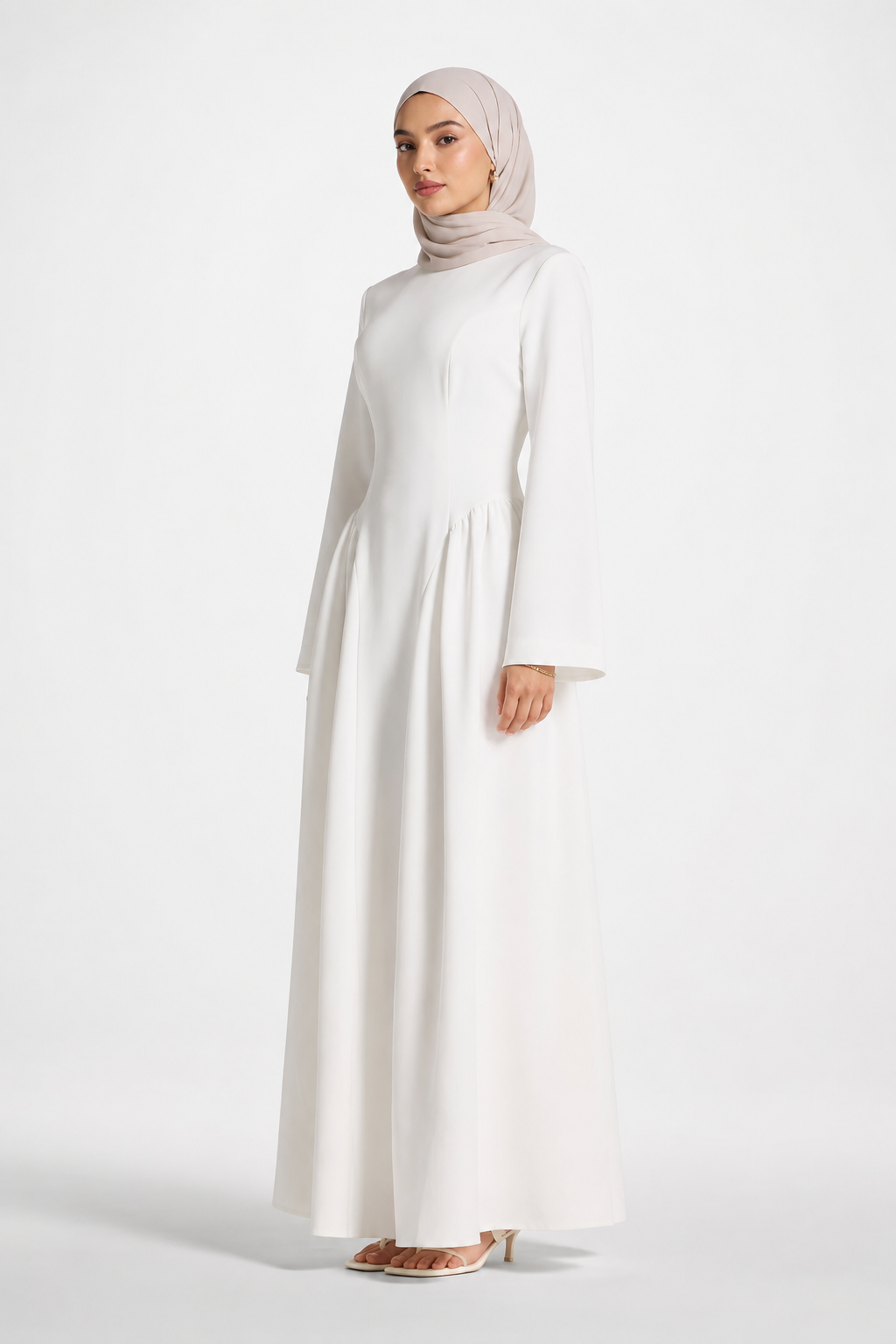 Woman wearing a long white dress and beige hijab on a white background