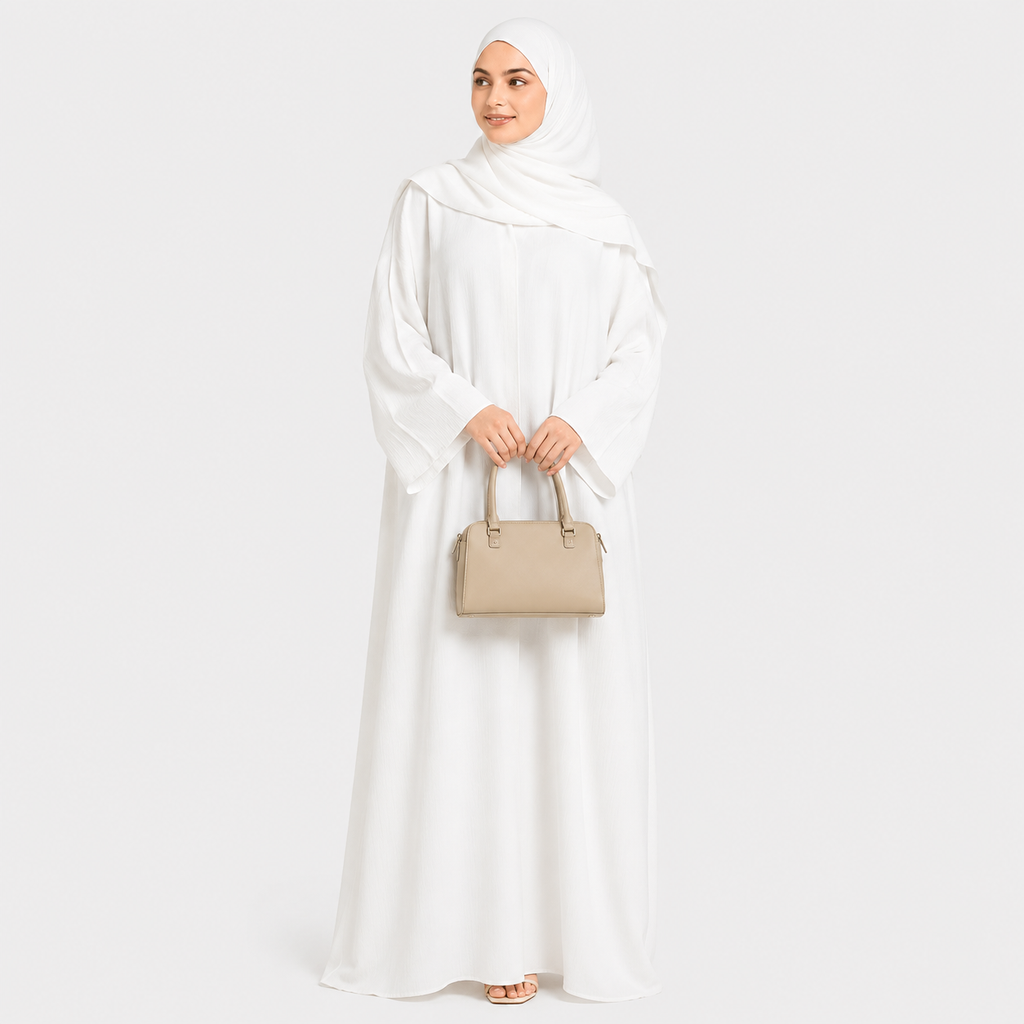 Woman in a white abaya holding a beige handbag on a white background