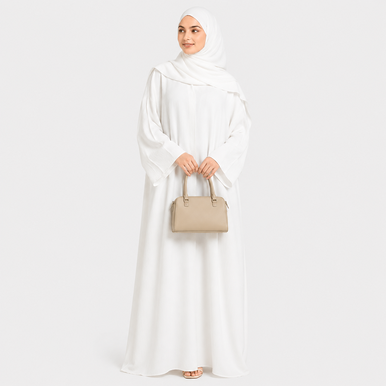 Woman in a white abaya holding a beige handbag on a white background