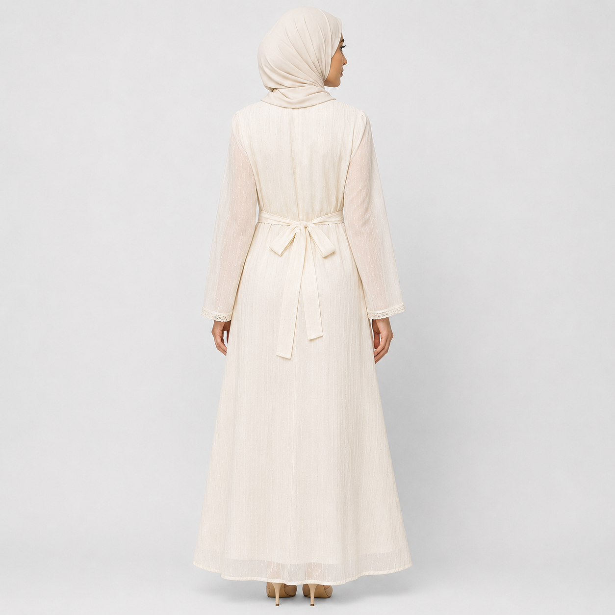 A woman wearing a long cream-colored modest maxi dress with a matching hijab, shown from the back against a light gray studio background.