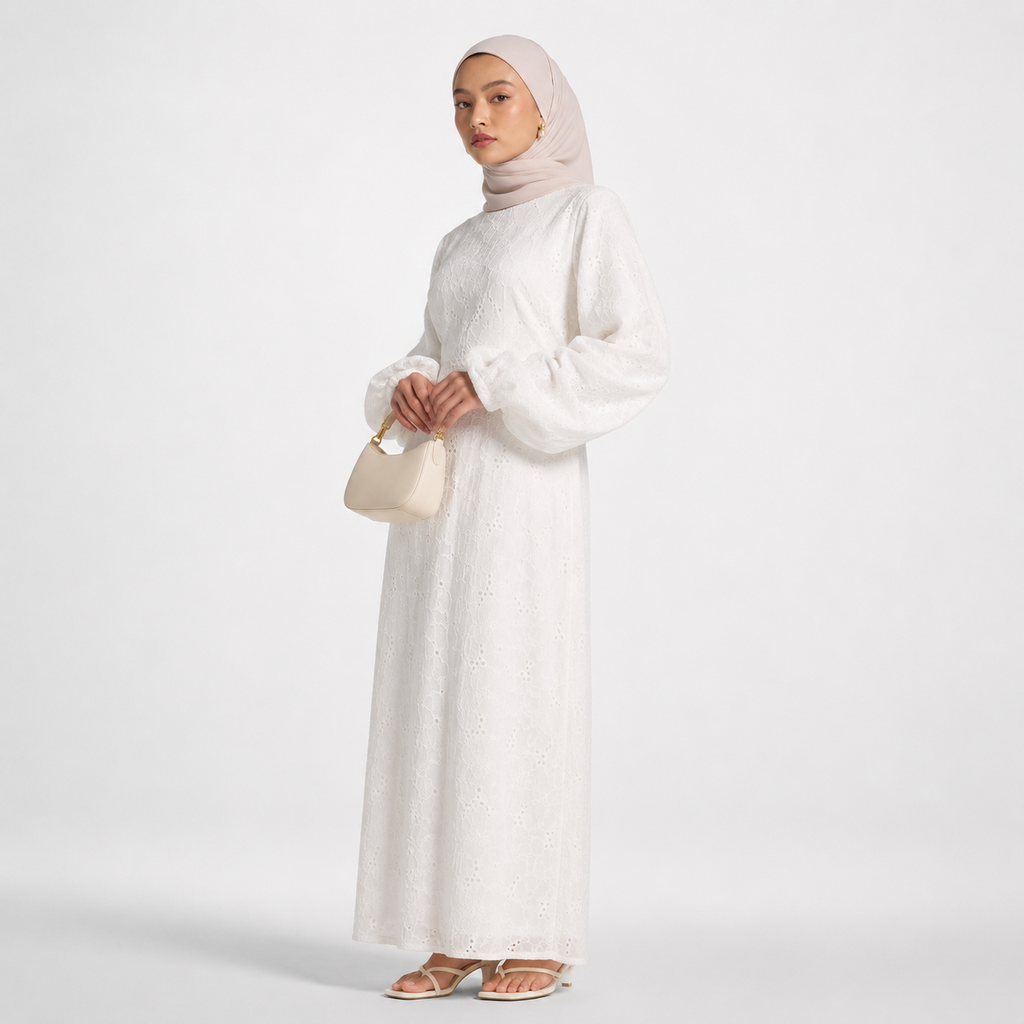 Woman wearing a long white dress and hijab holding a beige handbag on a light gray background