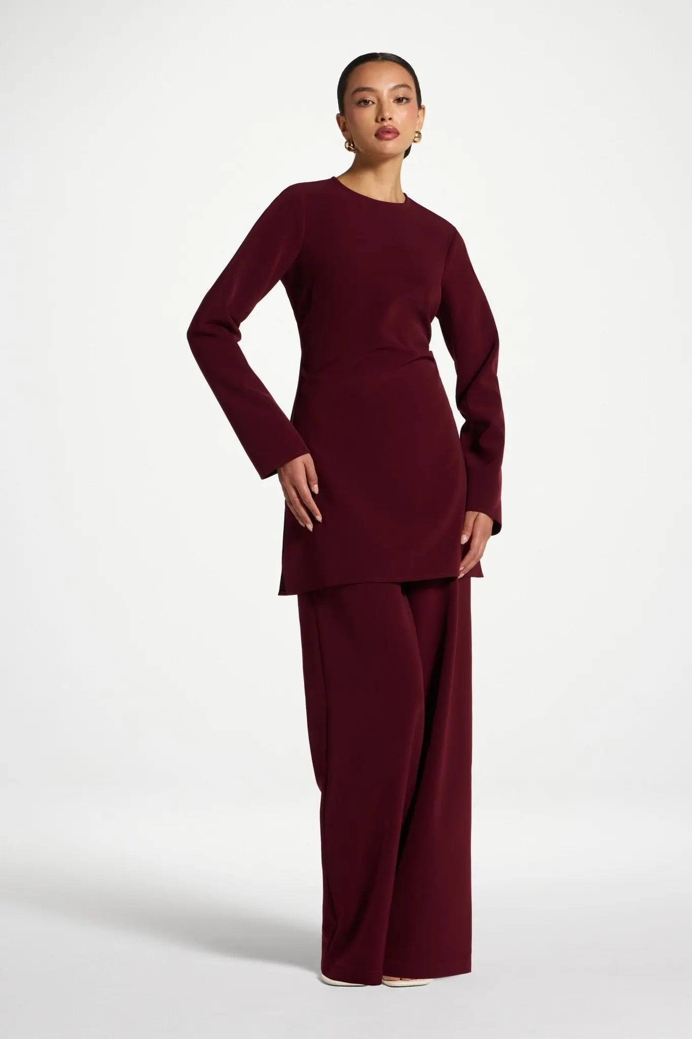Woman wearing a burgundy dress with a draped effect on a white background