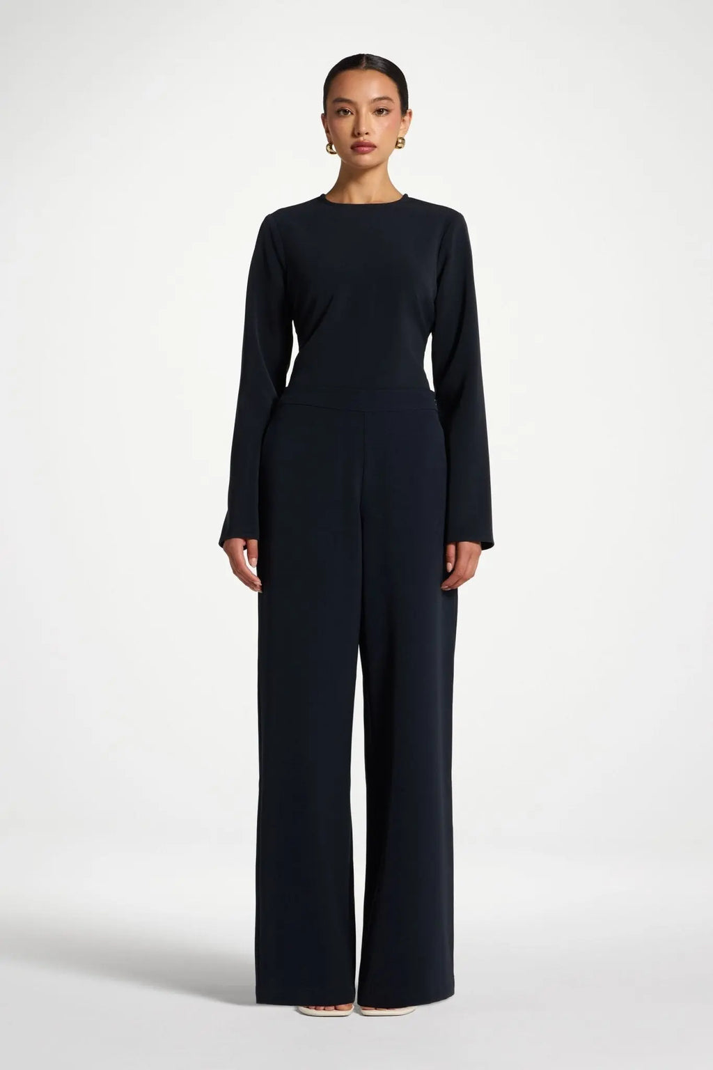 Woman wearing a black long-sleeve top and wide-leg pants on a white background