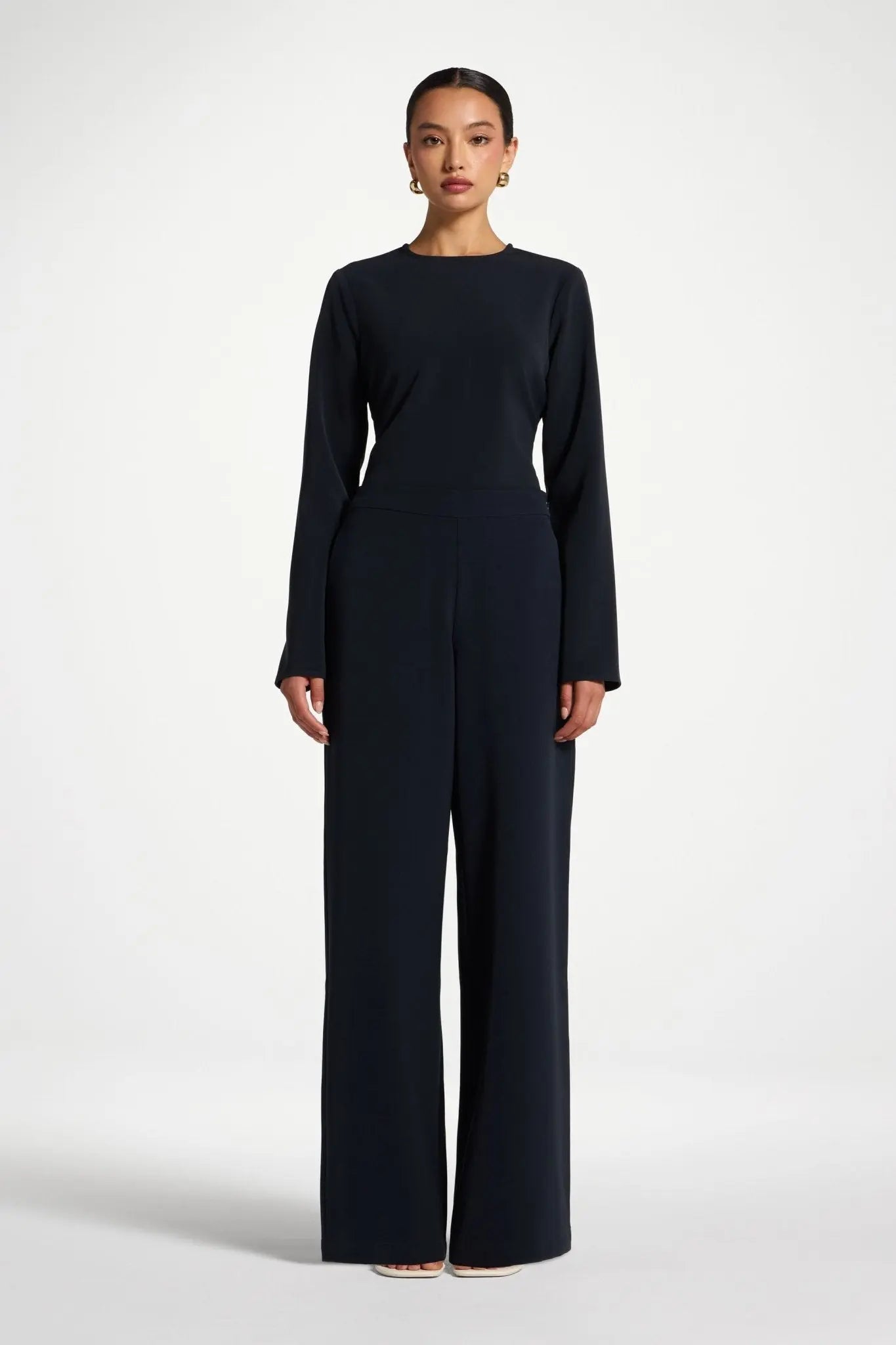 Woman wearing a black long-sleeve top and wide-leg pants on a white background